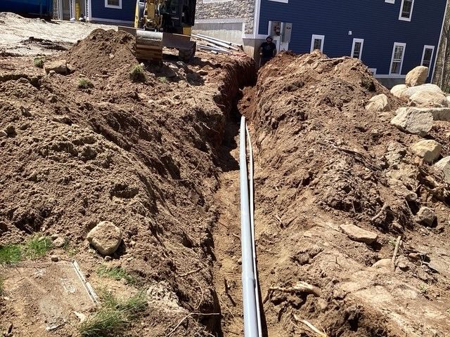 Narrow trench dug beside a new house, with pipe laid along the bottom