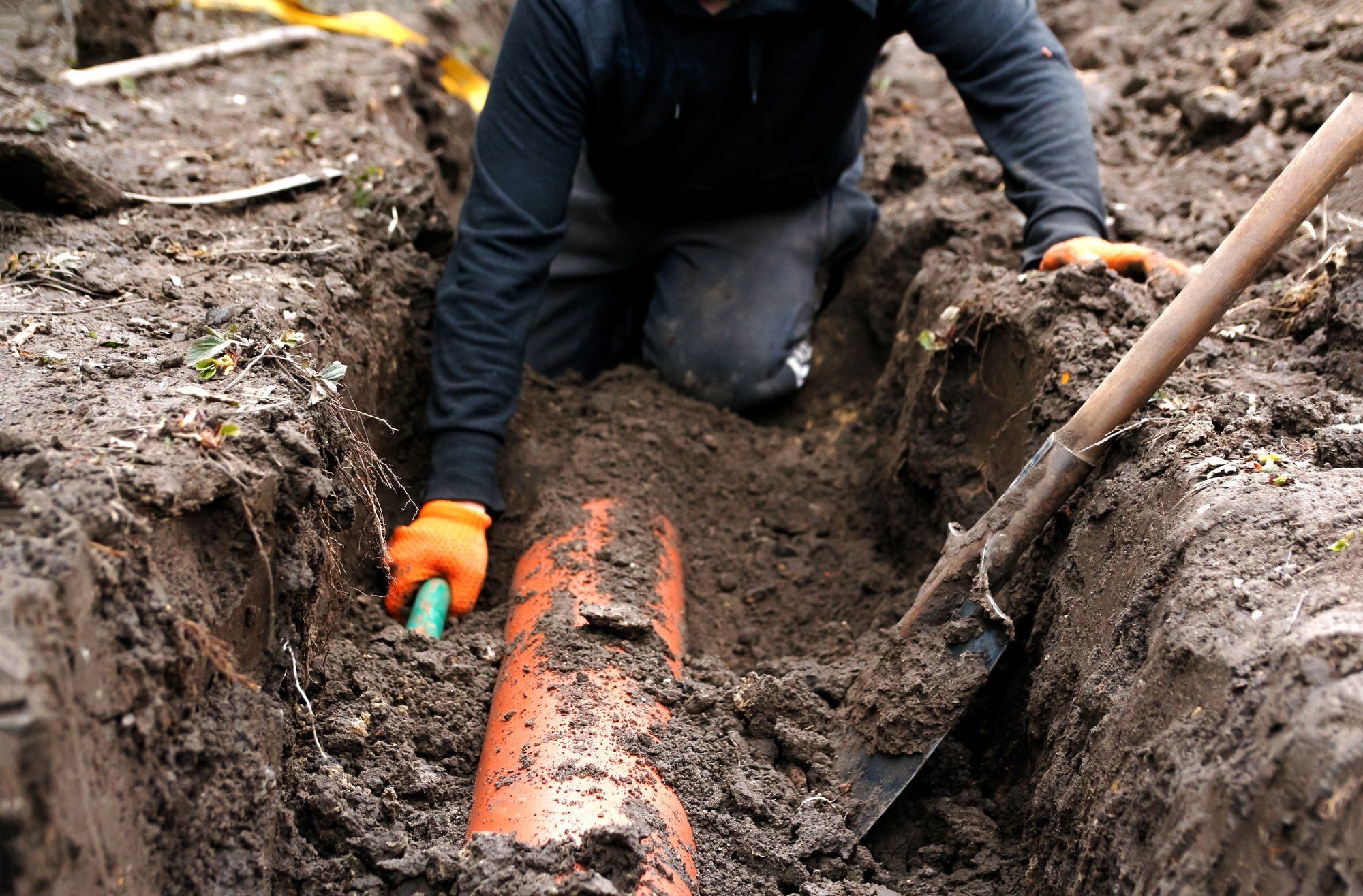 French drain installation: drain pipe being laid in a narrow trench