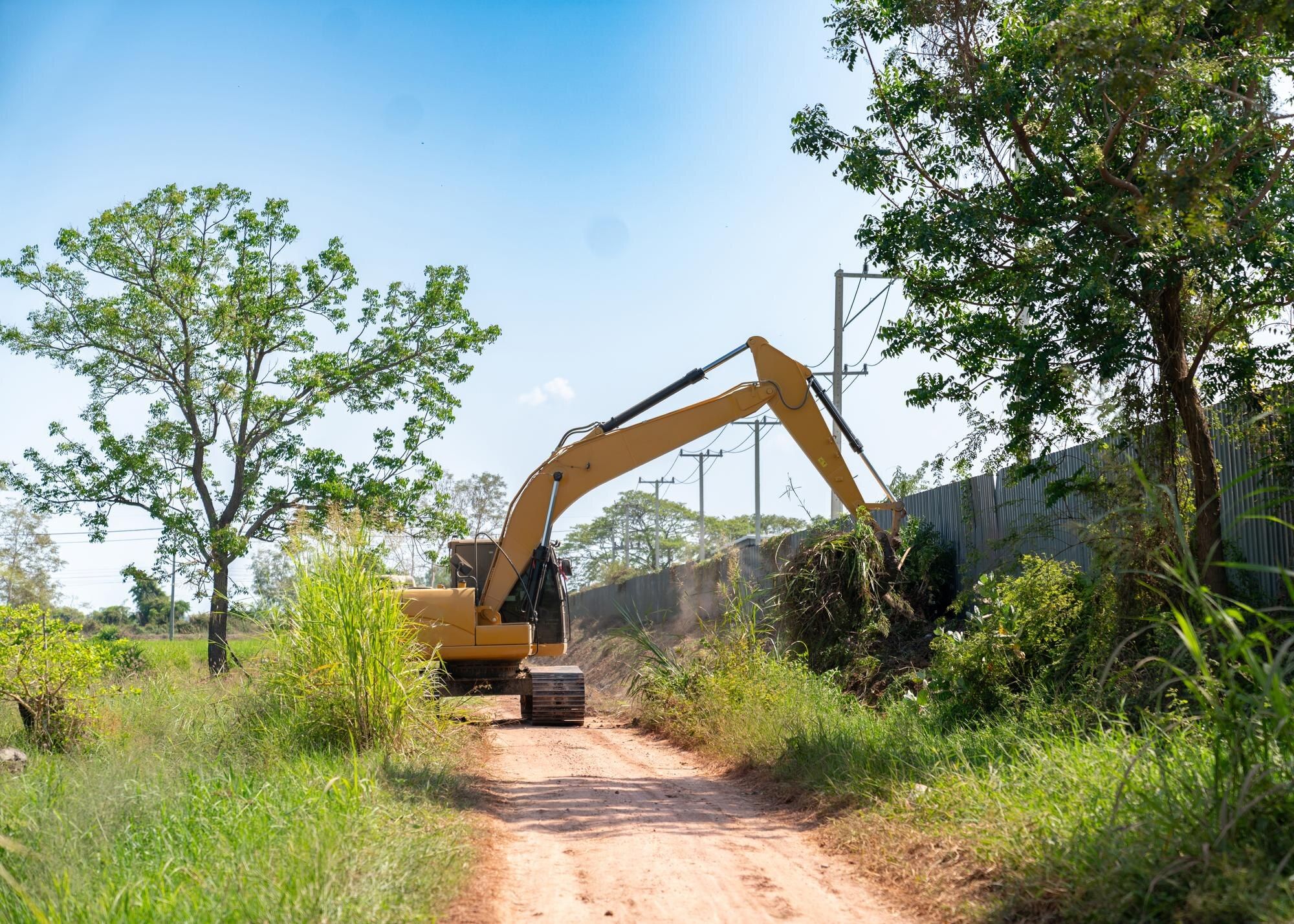Excavator clearing brush beside a dirt road