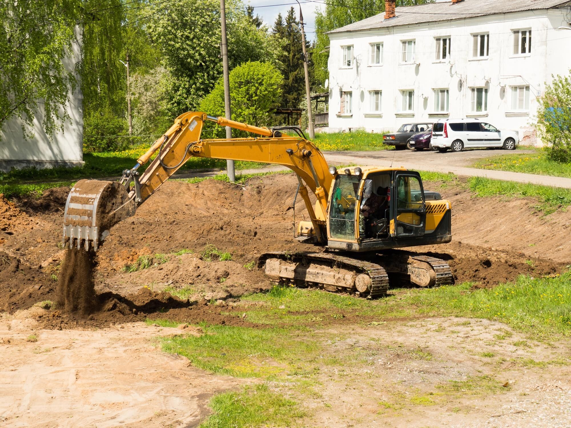 Yellow excavator digging up a grassy lot near houses