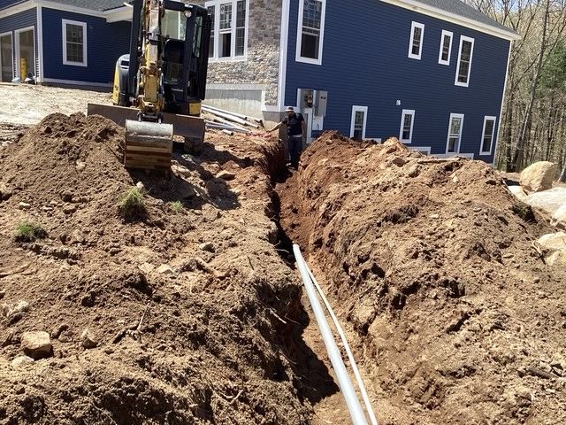 Dig Works mini excavator digging a narrow trench beside a house